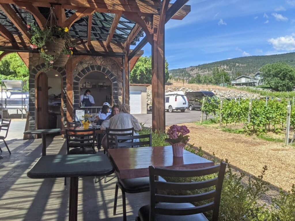 Serendipity Winery patio view with tables next to vineyard, bistro kitchen behind. The parking area is visible to the right