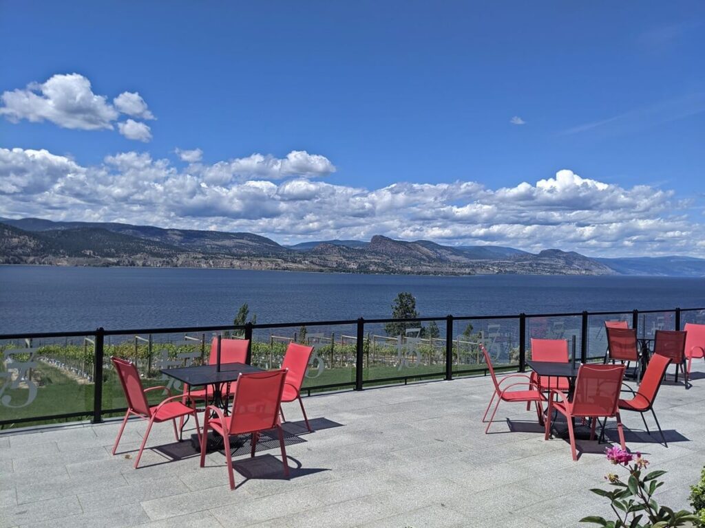 Bench 1775 patio view with multiple table and chair sets on large elevated patio, in front of vineyard and Okanagan Lake views