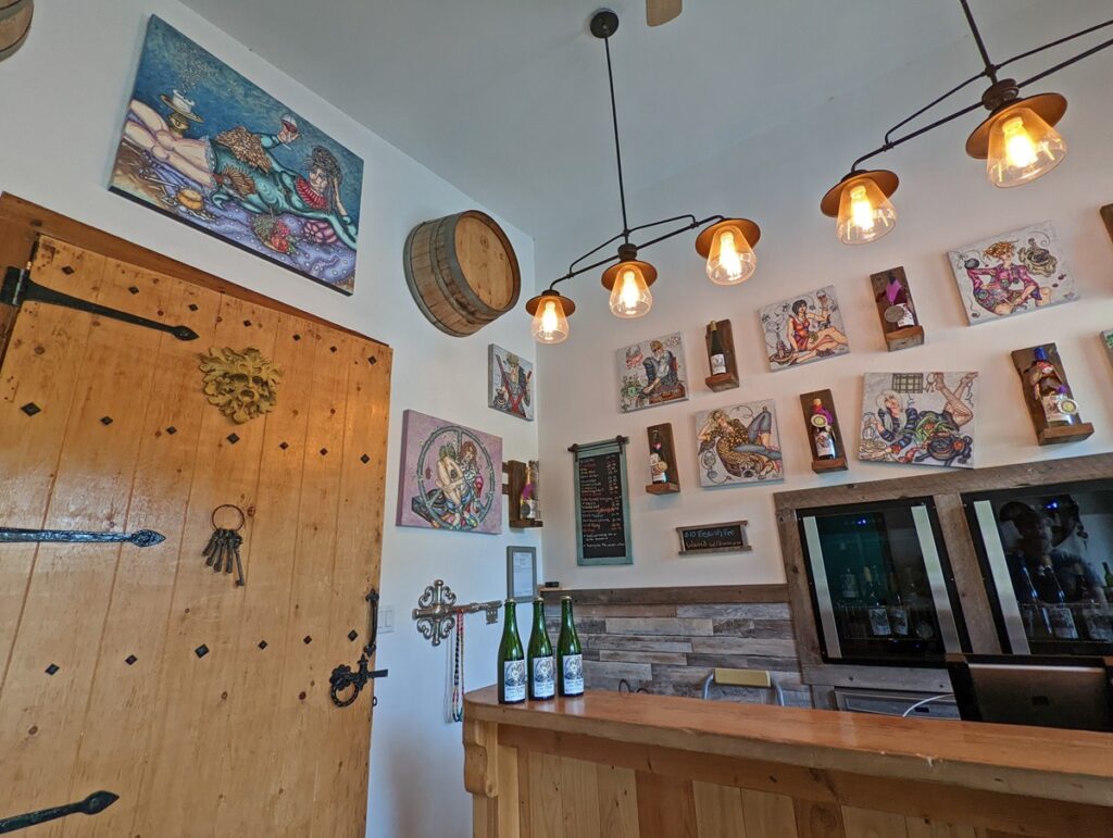 Crescent Hill Winery interior with wooden bar on right, large wooden door on left, hanging lighting, whimiscal paintings on wall