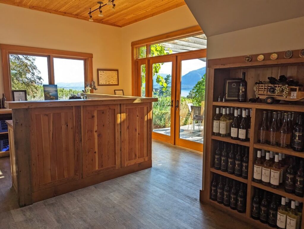 Interior look of Deep Roots Winery tasting room with wooden bar, large floor to ceiling door/window and wine bottle case