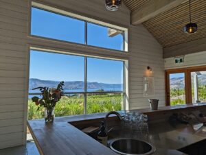 Joie Farm tasting room featuring a modern bar looking out to floor to ceiling window with views of Okanagan Lake visible in background