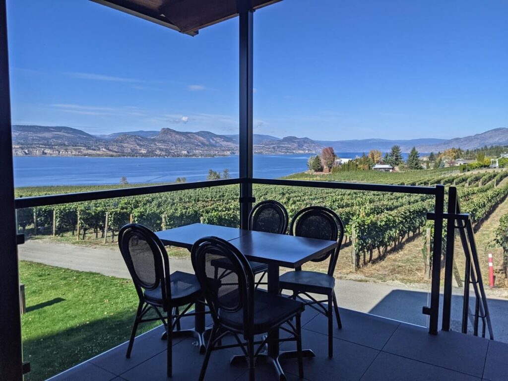 Patio views at Moraine Winery with table and four chairs on elevated platform above vineyard and Okanagan Lake views
