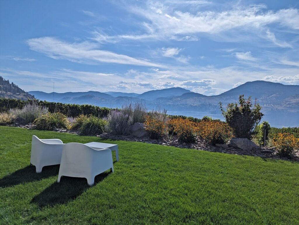 Views from Painted Rock Estate Winery with two low chairs and table on lawn in front of gardens, with lake and mountains visible behind