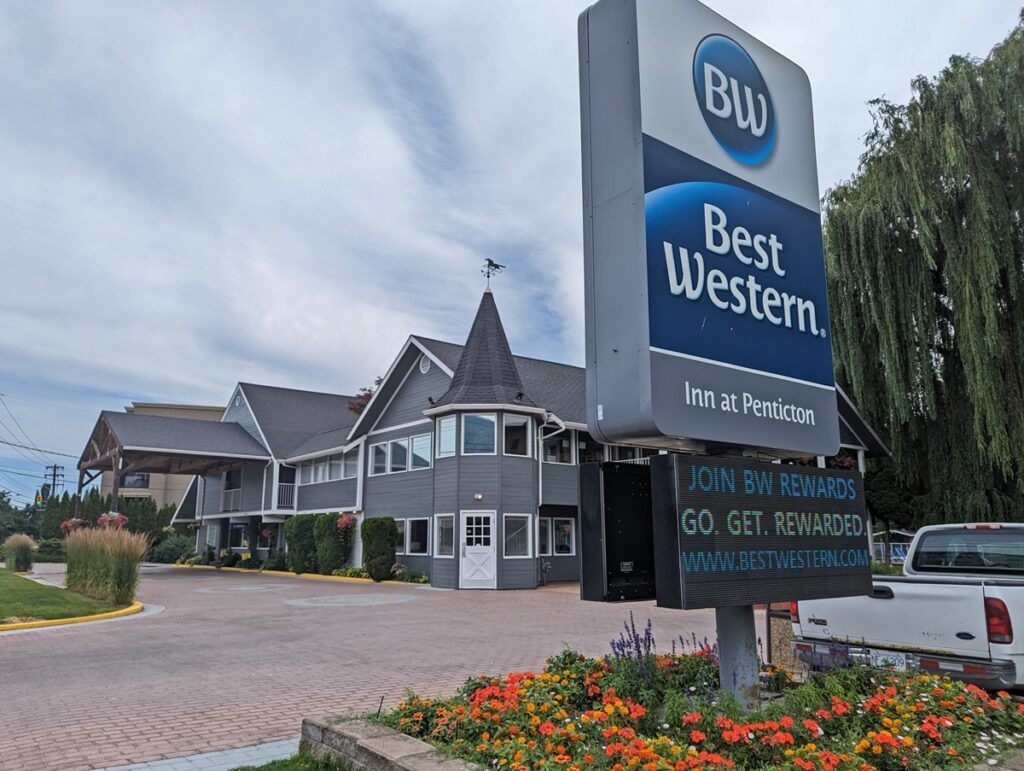 Penticton Best Western Inn with large signage on right above flowerbed. Grey hotel building to left