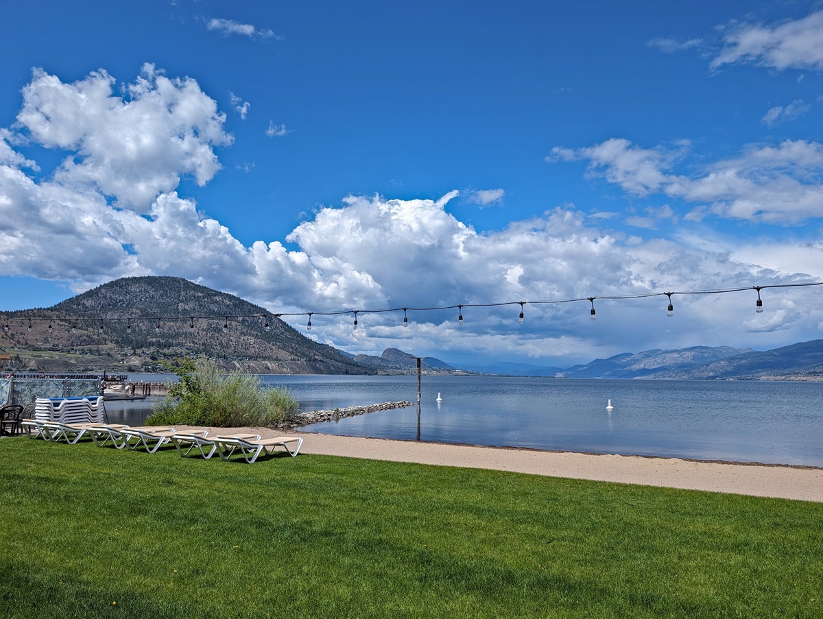 Looking across grassy lawn area to sandy beach next to calm Okanagan Lake - Penticton Lakeside Resort private beach