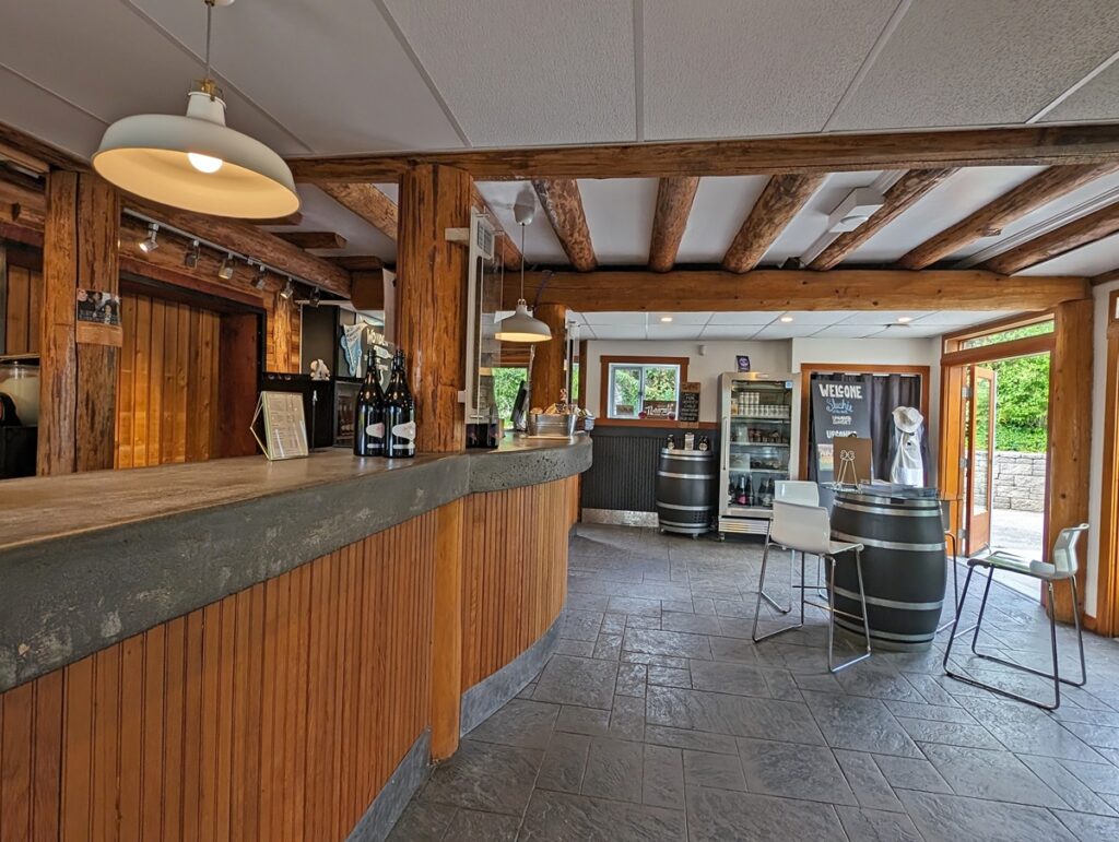 Elephant Island's indoor tasting space with wooden bar on left and seating around wine barrel on right. There are wooden beams visible in the ceiling