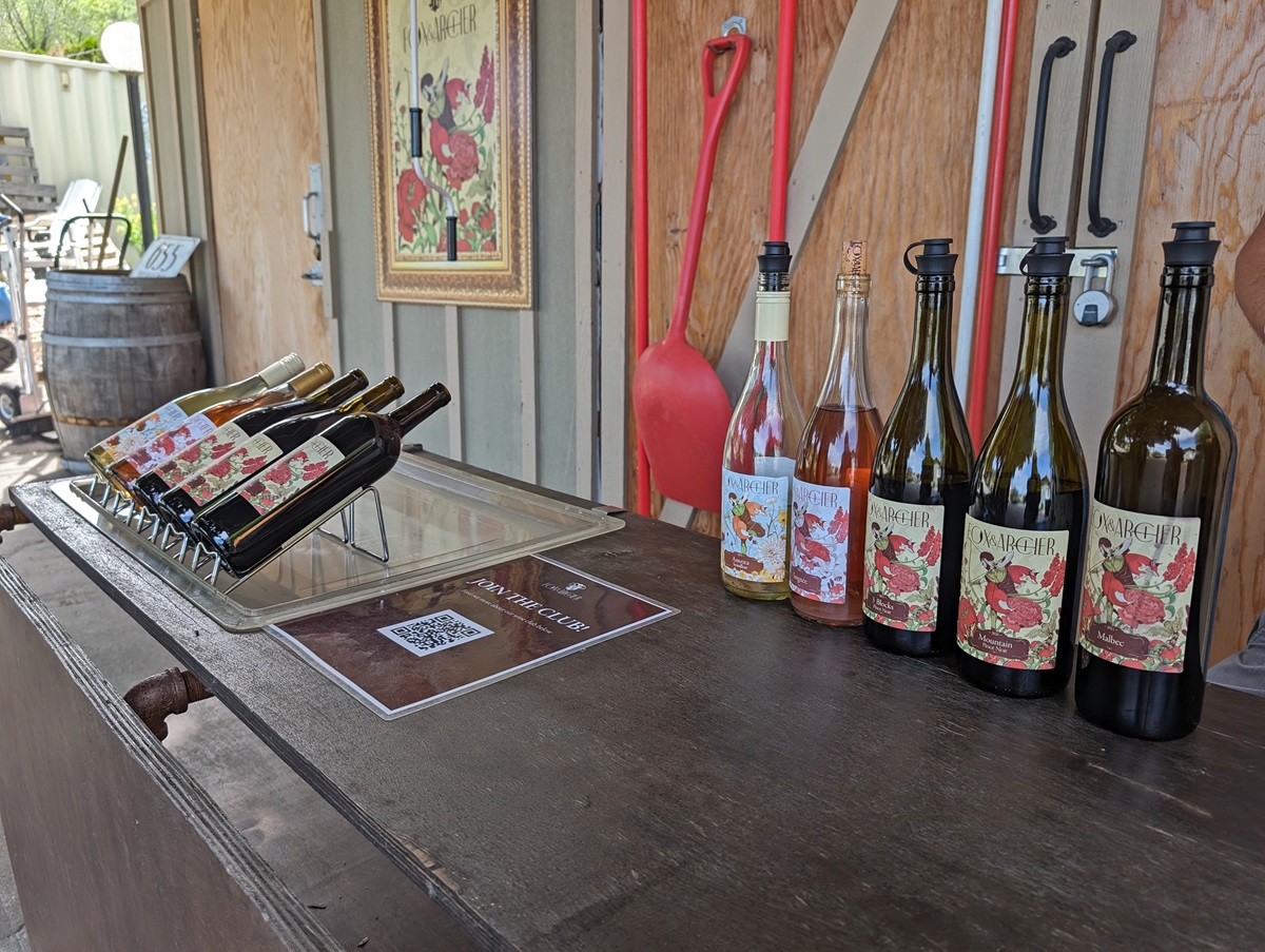 Close up of Fox and Archer Winery wine bottles lined up on rustic tasting bar with more on rack on left