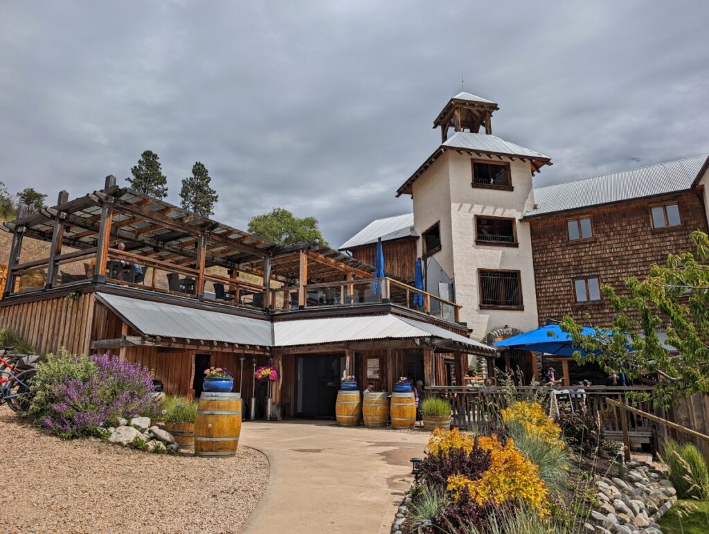 Looking up at the iconic Hillside Winery tower in centre, with second floor patio on left and first floor patio on right. Wine barrels line the path leading to the front door