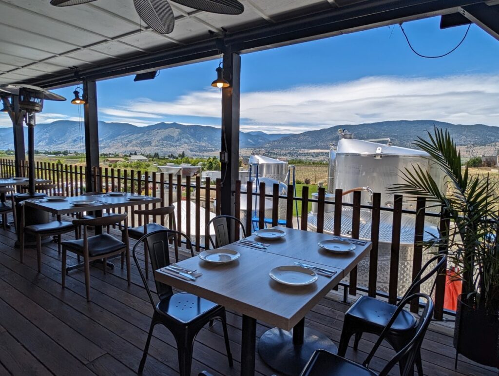 Side view of the Kitchen's scenic patio with set tables and chairs on covered wooden deck, looking out to mountainous view