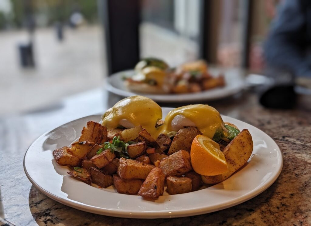 Close up of Eggs Benedict dish at the Bufflehead Cafe, featuring crispy hashbrowns in the foreground and two eggs covered in hollandaise in the background