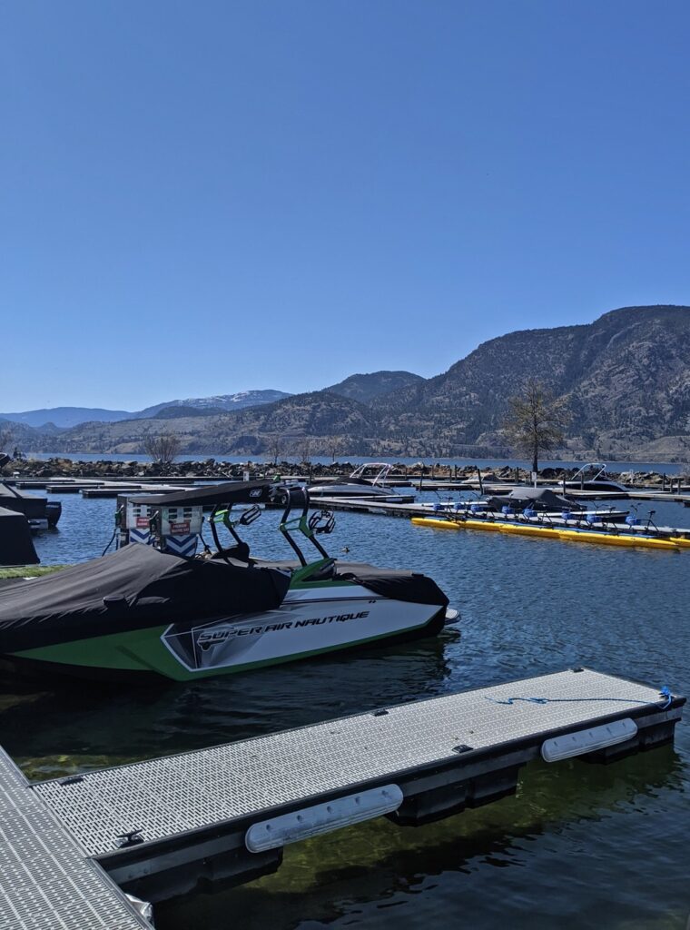 Marina views from Dragonboat Pub, with floating walkways and speed boats parked. There are forested hills behind the lake