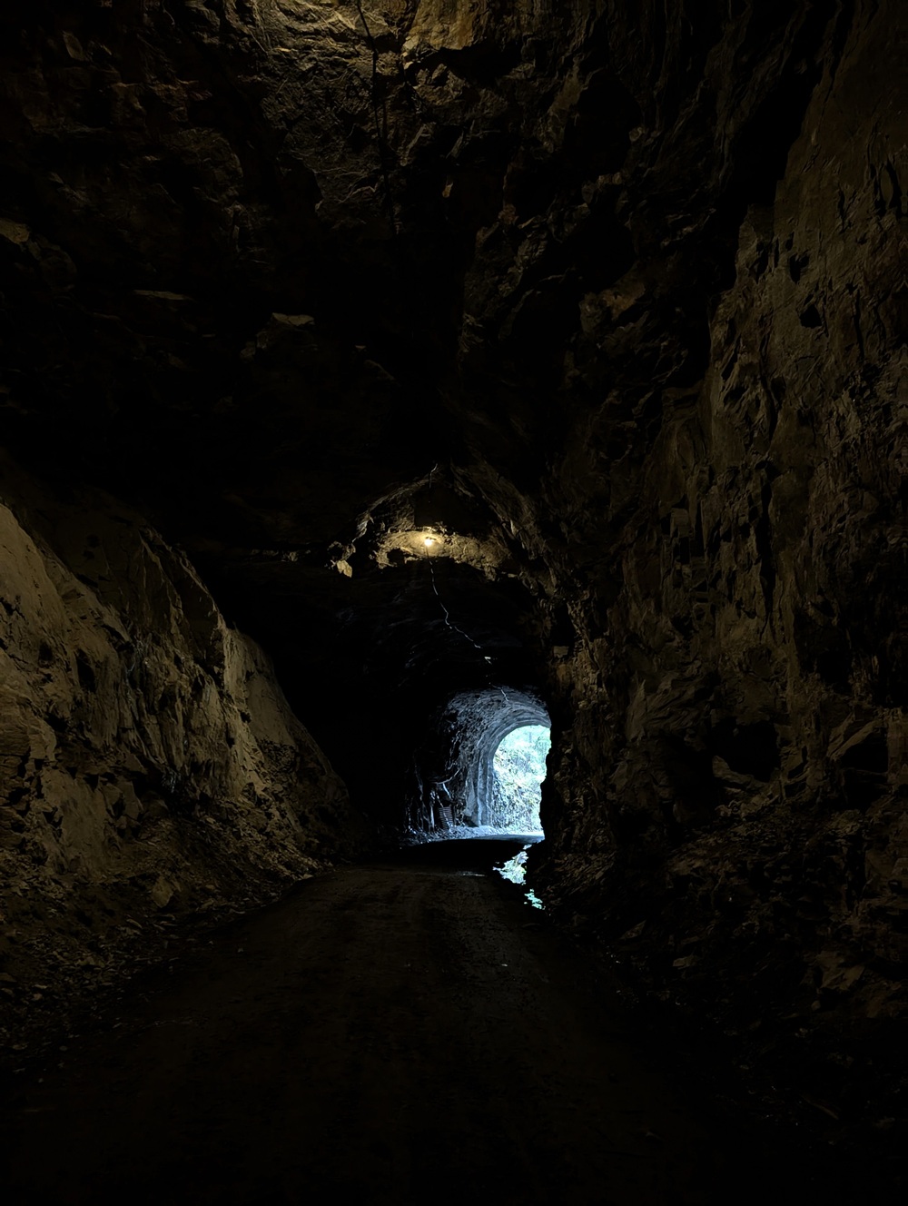 Dark interior view of Adra Tunnel with limited lighting, rugged rock walls and northern entrance visible in distance