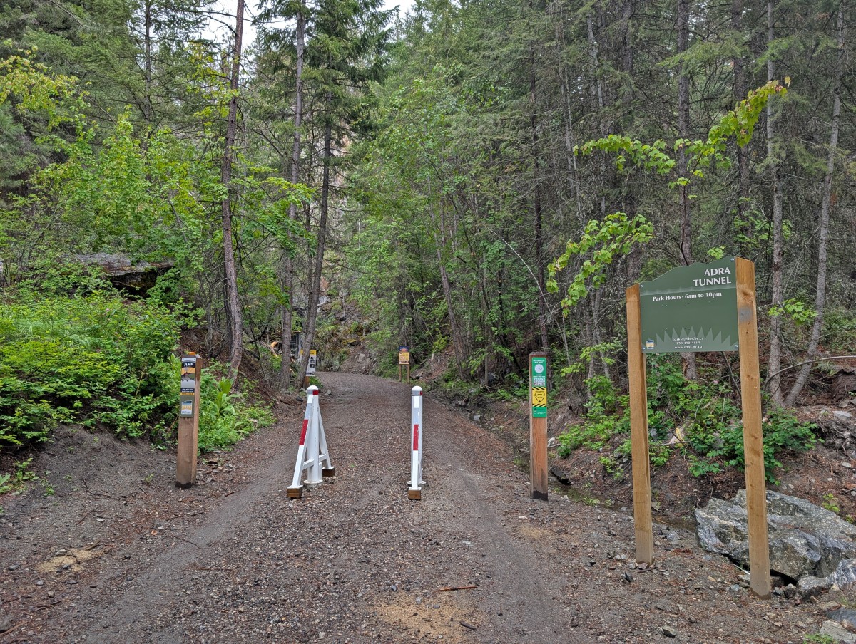 Adra Tunnel signage on trail with park hours (6am to 10pm), KVR graphics, warning signs. The wide trail is surrounded by forest