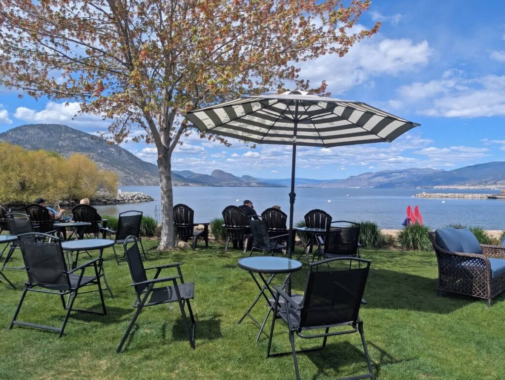 All Roads Cafe patio, featuring dark coloured furniture on lawn in front of lake views