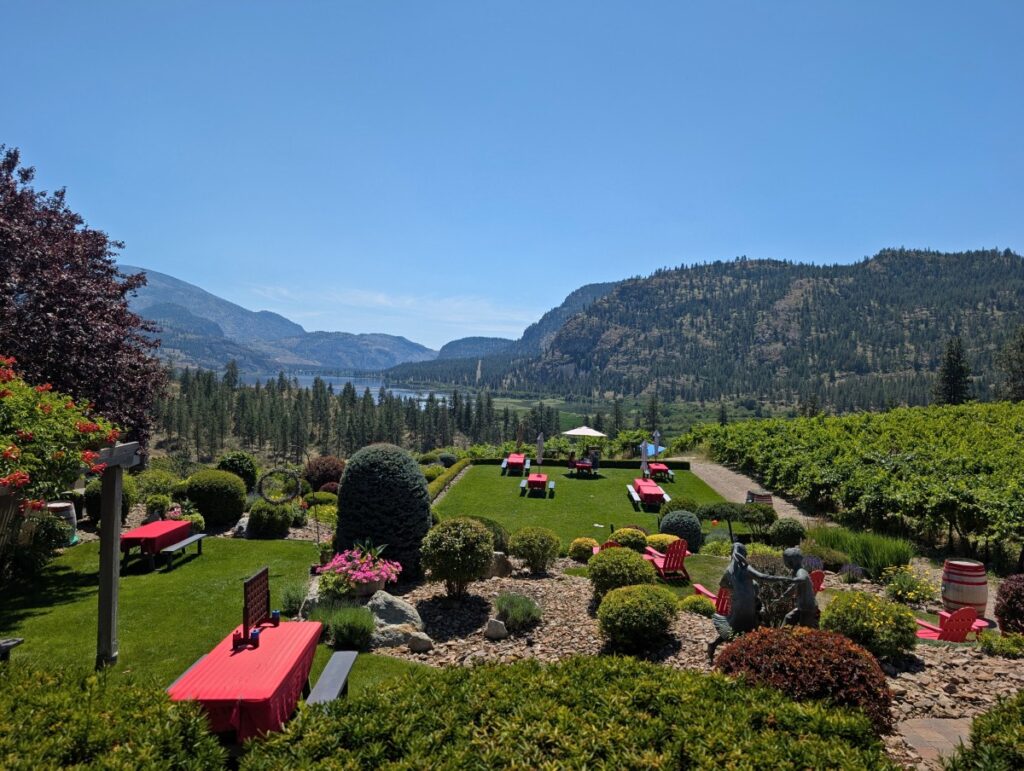 Elevated view looking down to Noble Ridge picnic area, which features grassy and landscaped garden sections and scattered picnic tables. There are views of a lake and forested mountains in the background