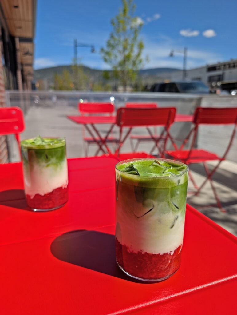 Close up of two glasses on red table outside Soe Cafe in Penticton, both featuring three layered Matcha Latte drink