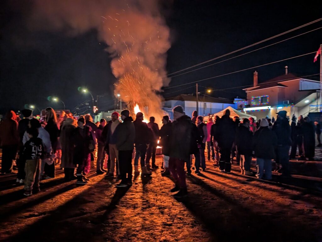Night view of bonfire at Oliver Light Up Christmas event, featuring lots of people standing in front of lit up bonfire