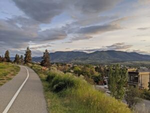 View of paved KVR Trail in Penticton, looking down on the city and forested mountains in the background