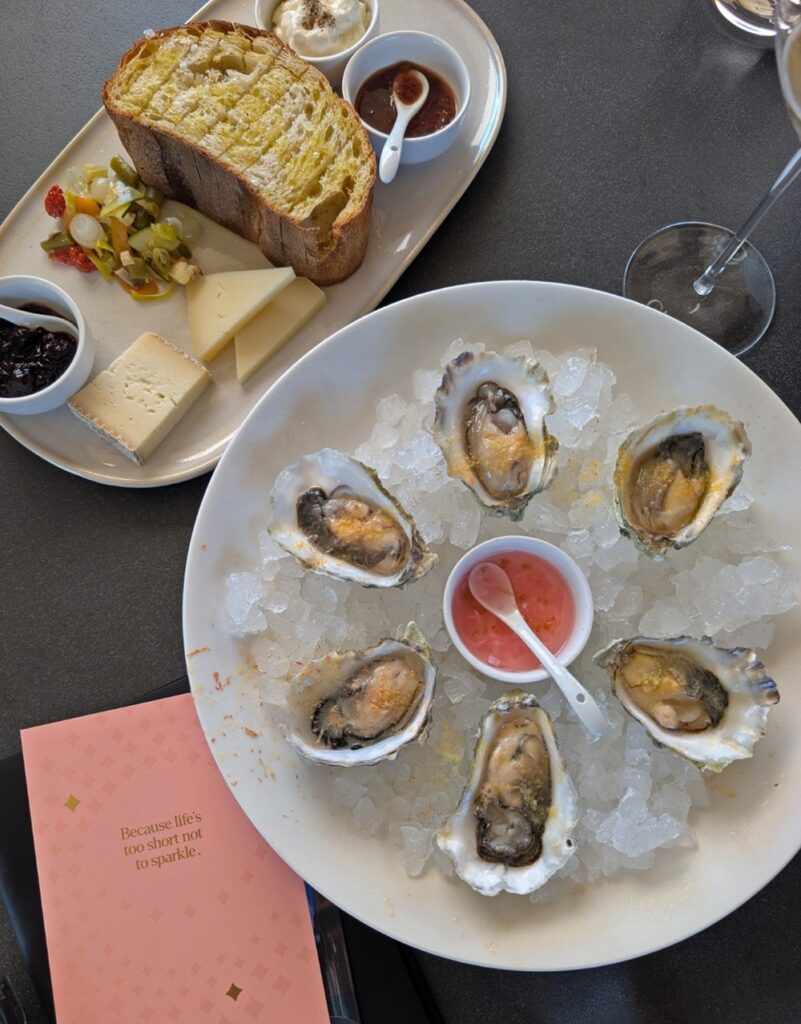 Overhead view of plate of oysters at Evolve Sparkling House, along with cheese plate featuing bread, jams and pickles