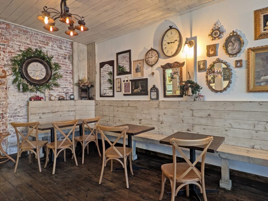 Interior of Petrasek Bakery, with wooden floors, wooden bench seats, whimsical chairs and a wall full of clocks and classic frames with black and white photos